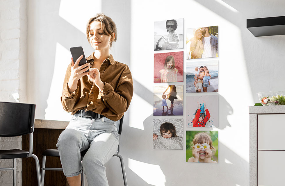 A person sits on a chair in front of eight Snapfish Photo Tiles featuring family photos on a wall next to a dresser