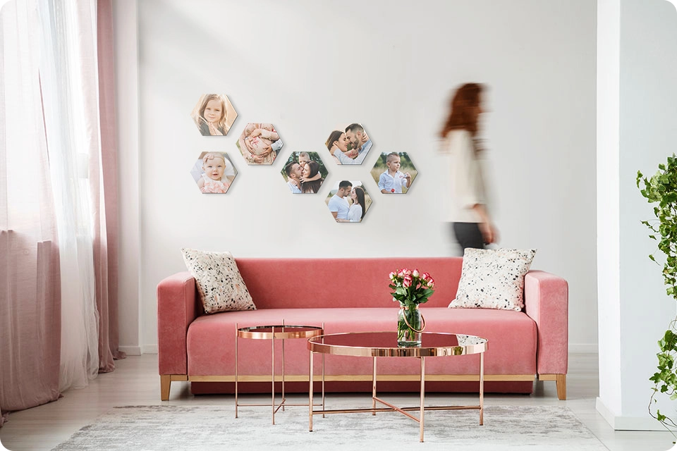 Woman walks by a set of multiple Snapfish Photo Tiles in a checked pattern on a wall featuring family photos above a pink sofa